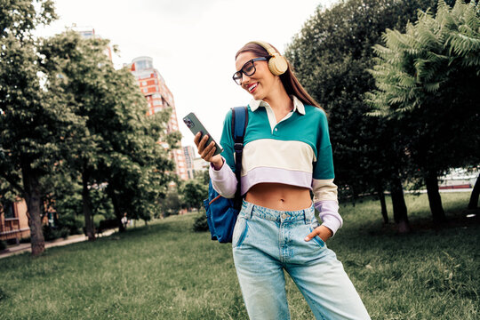 Young woman enjoying outdoor leisure with headphones and smartphone in a vibrant urban park setting