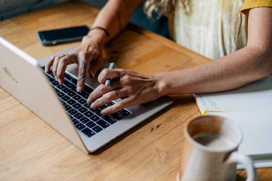 Hands typing and writing notes at laptop on wooden desk - Powered by Adobe
