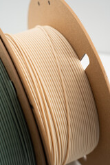 Rolls of muted green and beige PLA 3d printer filament on environmental friendly cardboard roll...