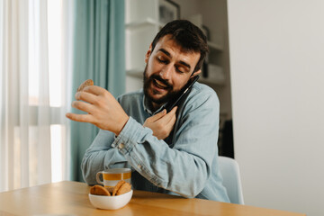 Happy man at home eating cake and having a phone conversation