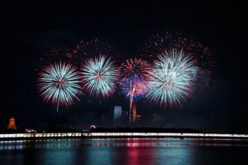 Spectacular Fireworks Display Bursting Over Illuminated City Skyline and Bridge Reflected in Water at Night