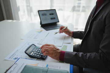 Businessman analyzing financial charts and using calculator in office