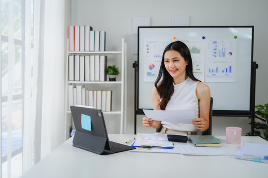Asian businesswoman having video conference using tablet and showing financial report in modern office