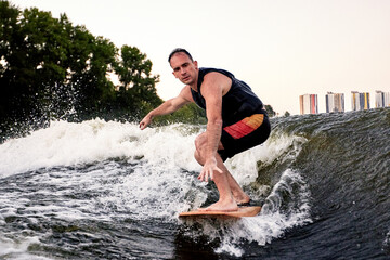 Young athletic man vigorously rides a wakeboard. Handsome guy in black swimsuit glides...