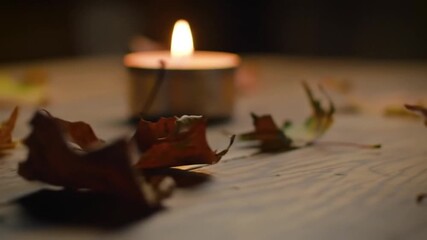 A single lit tealight candle casts a warm and soft glow on scattered dry autumn leaves on a rustic wooden table, creating a cozy hygge atmosphere - Powered by Adobe