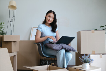 Female Asian using laptop amid relocation boxes preparing for move
