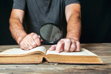 A man uses a magnifying glass while examining an old book. Concept of research, investigation,...