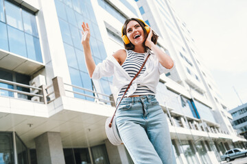 Young woman enjoying music while walking on a sunny urban street