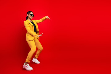 Joyful woman in yellow suit dancing against vibrant red background, expressing positivity and energy, showcasing elegance