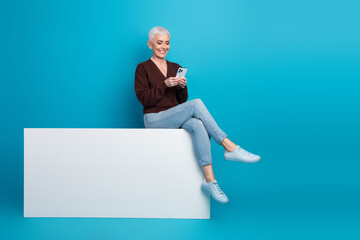 Elderly woman using smartphone against blue background showcasing leisure and modern lifestyle with...