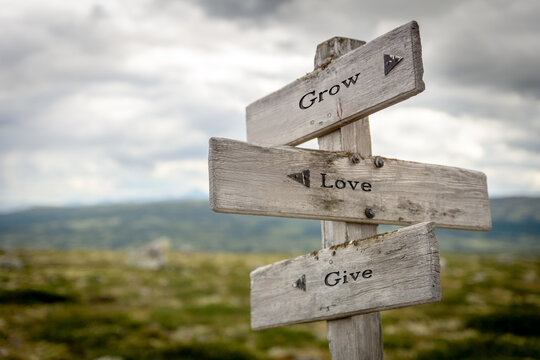 Wooden sign on a mountain plateau with the quote "Grow Love Give", surrounded by natural alpine scenery and gentle sunlight, conveying inspiration, kindness, and personal growth.