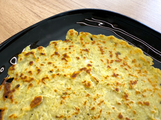Golden brown potato pancake served on black plate, traditional homemade dish placed on wooden table.