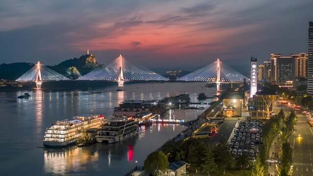Yichang China cable-stayed bridge over Yangtze River at sunset with illuminated cruise ships and city skyline waterfront