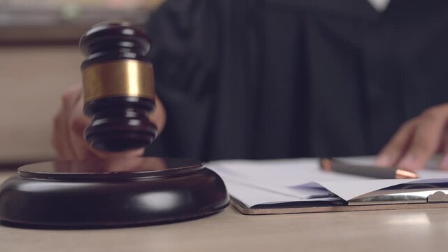Close-up of judge hand holding gavel about to strike on desk beside legal documents. Symbol of justice, authority, and decision.