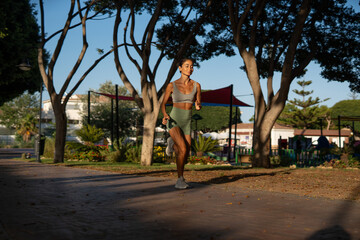 Slim athletic woman running outdoors on a sunny morning in the park, dressed in green shorts and...