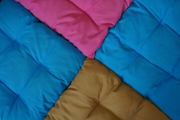 Title: An abstract, close-up view of four colorful, quilted cushions meeting at a central point,...