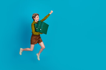 Cheerful young businesswoman jumping in casual attire holding green folders against a vibrant blue...