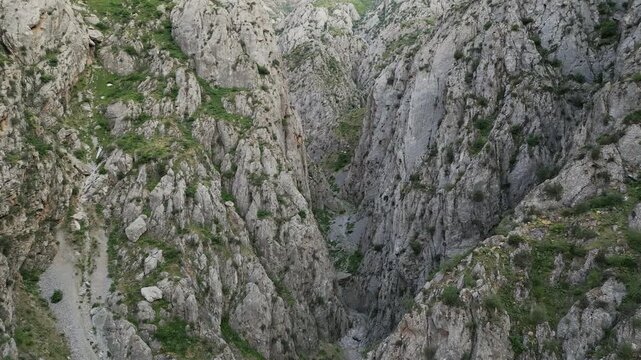 Aerial view follows a canyon corridor in Uzbekistan as the drone floats over rugged cliff and gravel fan, revealing bends and fresh greenery. Golden sunrise lights the Chatkal range and ravine