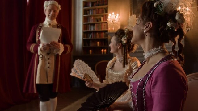 Medium shot of young 19th century Caucasian gentleman serenading two mature ladies with own song and reciting poems, while excited noblewomen are listening, waving fans and admiring talent