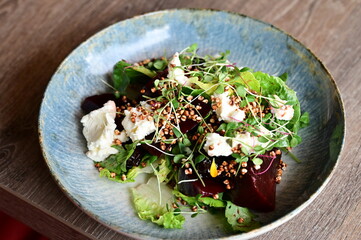 Close-up view of a salad with roasted beetroot, cheese, and fresh herbs, served on a plate in a restaurant on a wooden table.