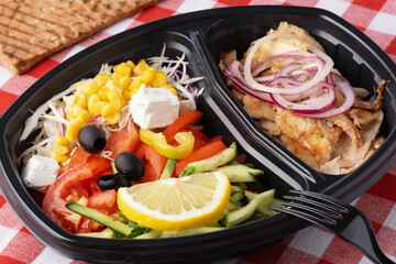 Colorful salad and grilled chicken in a black takeout container on a red and white checkered table