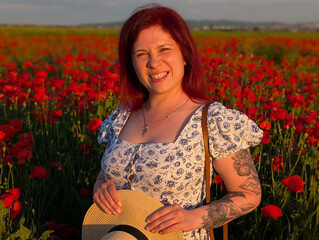 A woman smiles brightly in a poppy field with sunset light on her face. Portrait of happiness,...