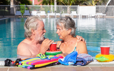 Happy senior couple relaxing together at a swimming pool, smiling and embracing at the poolside....