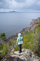 Person in green jacket overlooking rocky shoreline under overcast sky in White Sea, Karelia,...