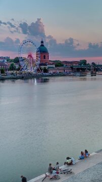 Aerial view of La Grave Hospital with Saint-Pierre Bridge. Port de la Daurade park along the Garonne River timelapse in Toulouse, France. Sunset colorful clouds, ferry at dock and riverside atmosphere