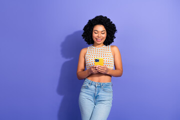 Trendy Woman Using Smartphone on Vibrant Purple Background in Casual Fashionable Outfit Displaying Relaxed Lifestyle