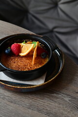 Close-up view of a tasty sweet dessert — crème brûlée served with fresh fruits on a grey background. A delicate caramelized cream dessert with a crunchy top, beautifully styled and served on a table,