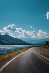 Scenic highway leading to a distant mountain range, beside a lake