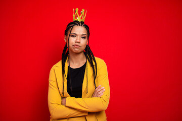 Confident young woman wearing a yellow suit posing with folded arms and a playful expression against a vibrant red background
