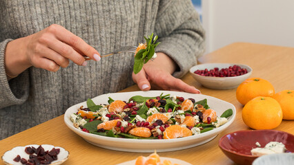  Woman eating winter salad with fresh spinach, mandarin and pomegranate at wooden table.