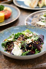 Close-up view of a salad with roasted beetroot, cheese, and fresh herbs, served on a plate in a restaurant on a wooden table.