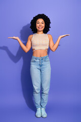 Happy young woman with curly hair in vibrant fashion poses against a purple background, expressing...