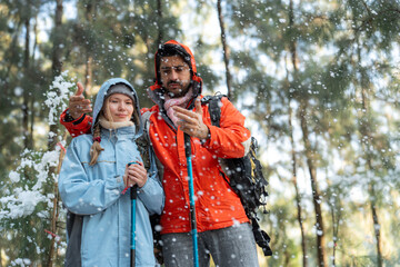 Adventurous Couple Exploring Snowy Forest Trail – Man Pointing While Woman Stands Beside with...