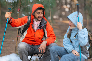 Couple Sitting in Snowy Forest – Man and Woman Engaged in Serious Conversation While Trekking in...