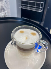 Coffee cup with layered espresso and milk foam, featuring playful face design, served on a black tray, creating a delightful and inviting atmosphere for coffee lovers
