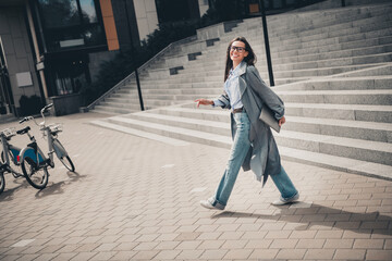 Young woman walking on urban street, smiling, wearing stylish gray coat, exploring the city...