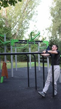 Vertical screen student struggles with calisthenics on parallel bars in outdoor park showing failed attempt at strength exercises while still practicing and improving skills