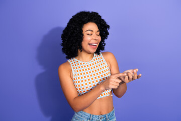 Young woman with curly hair laughing and pointing at something, captured against a vibrant violet...