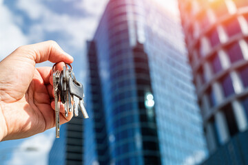 Hand Holding Keys Against Glass Office Towers – Concept of Property Ownership and Corporate Access