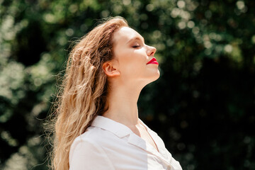 Obraz premium Beautiful young woman enjoying a sunny day outdoors with vibrant lipstick and relaxed expression, highlighting natural charm