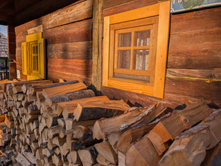 Piles of firewood near wooden house with colorful windows. Village lifestyle and architecture.