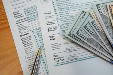 Obraz premium U.S. tax return documents with pen and dollar bills on table during financial filing process