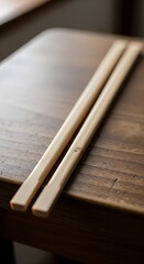 Two light beige bamboo chopsticks rest on a dark wooden surface.