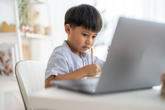 Asian boy studying with pencil at home smiling writing with notebook and school supplies, online learning, creative study in homeschooling, tutoring and learning course, kids education development