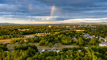 Queensbury, NY, USA - August 27, 2025: Late afternoon aerial view of a rainbow over the Queensbury / Glens Falls area near the southern boundary of the Adirondack Park of of Interstate 87.	