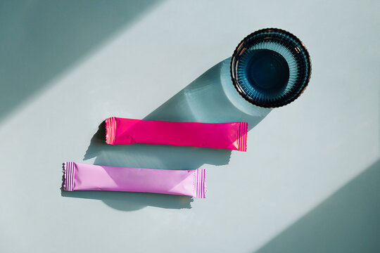 Two colorful sachets and blue glass with water on blue background.